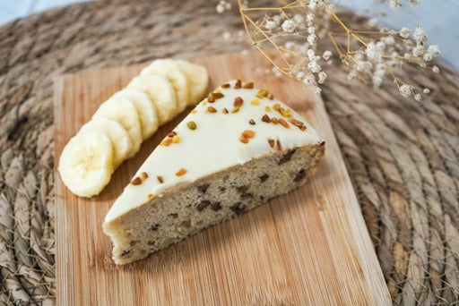 Close-up van een punt bananen pistache cake bedekt met een knapperige mix van pecannoten en pistaches. De cake heeft een lichte textuur en is doordrenkt met de smaak van rijpe bananen en pistaches. Een heerlijke traktatie voor elke gelegenheid!