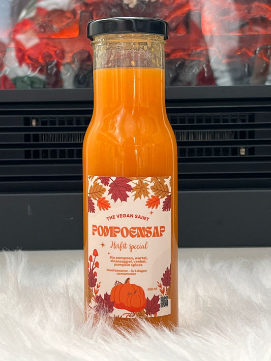  "Fles pompoensap van The Vegan Saint, gemaakt van pompoen, wortel, sinaasappel, venkel, peer en Pumpkin Spices, met een achtergrond van een brandende open haard."