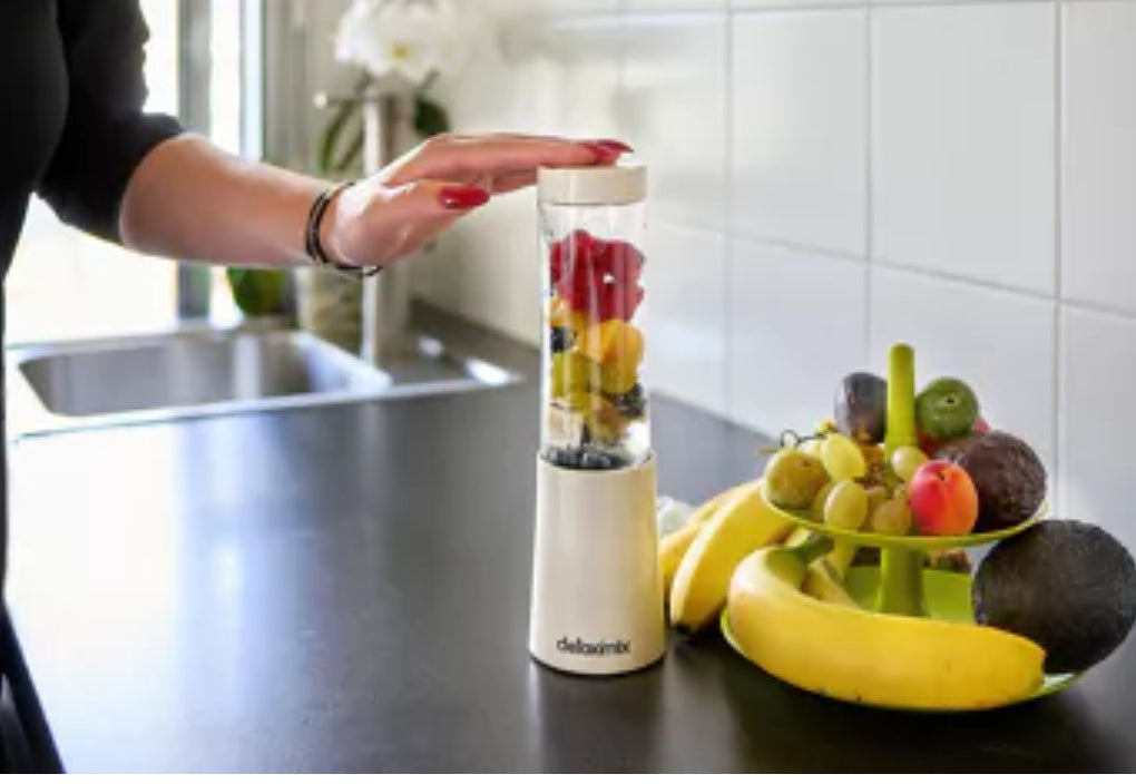 "Detoximix mini gebroken witte blender met twee transportflessen en receptenboek, ideaal voor gezonde smoothies onderweg. Dame heeft de blender gevuld met vers fruit, kaar voor het blenden."