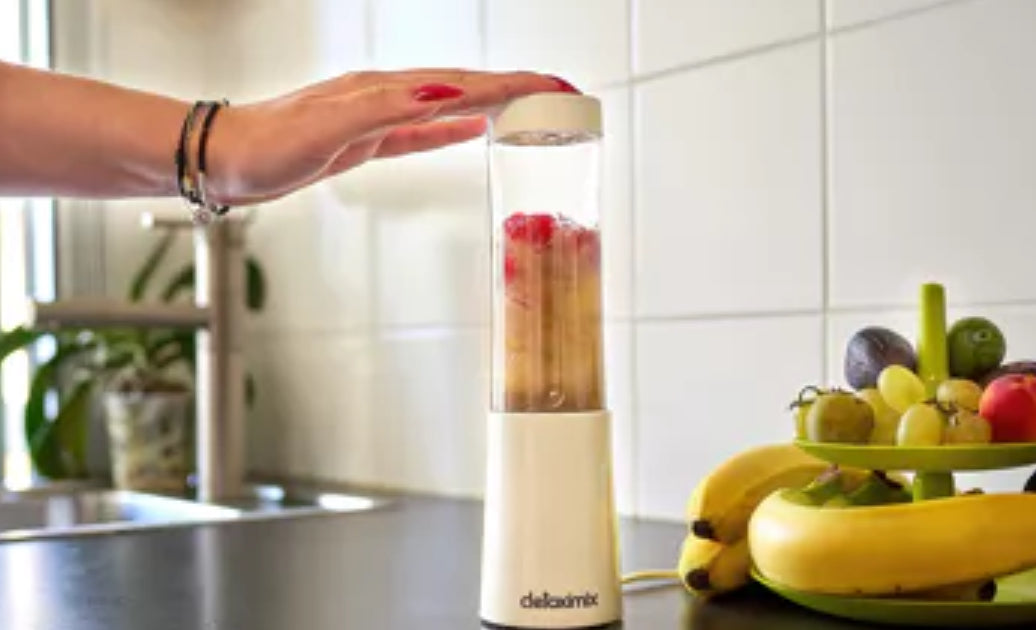 "Detoximix mini gebroken witte blender met twee transportflessen en receptenboek, ideaal voor gezonde smoothies onderweg. Dame heeft vers fruit geblend voor onderweg."