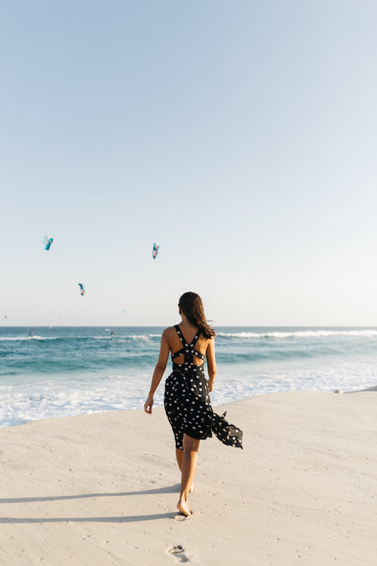 "Een vrouw staat op het strand en kijkt uit over de zee, terwijl ze geniet van een verfrissende duik tijdens een zomerse dag. Ze zit lekker in haar vel en voelt zicht zelfverzekerd na de Summer detox van The Vegan Saint.' 